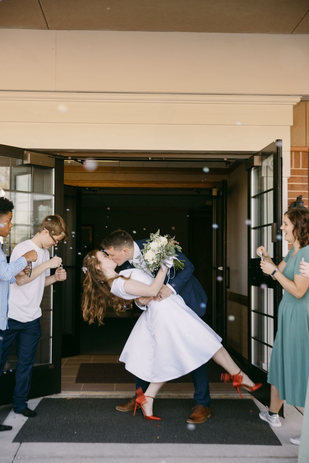 A couple performs a romantic dance dip sequence in a building hallway while others watch and take photos.