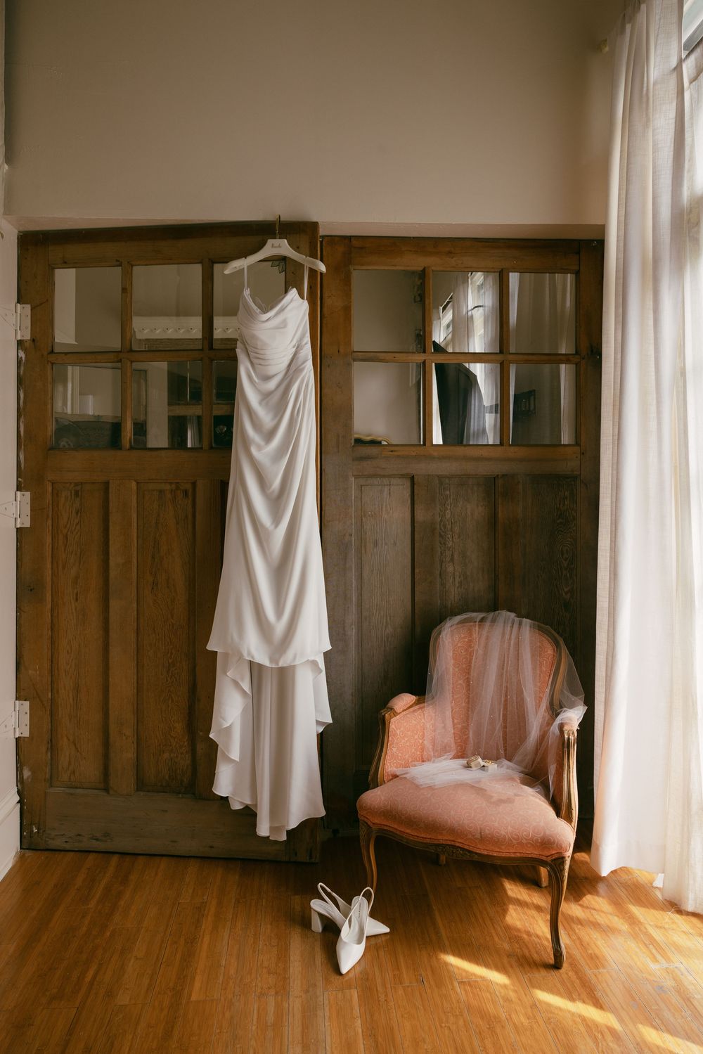 Wedding dresses hanging on display in a sunlit room with wooden walls and hardwood floors.