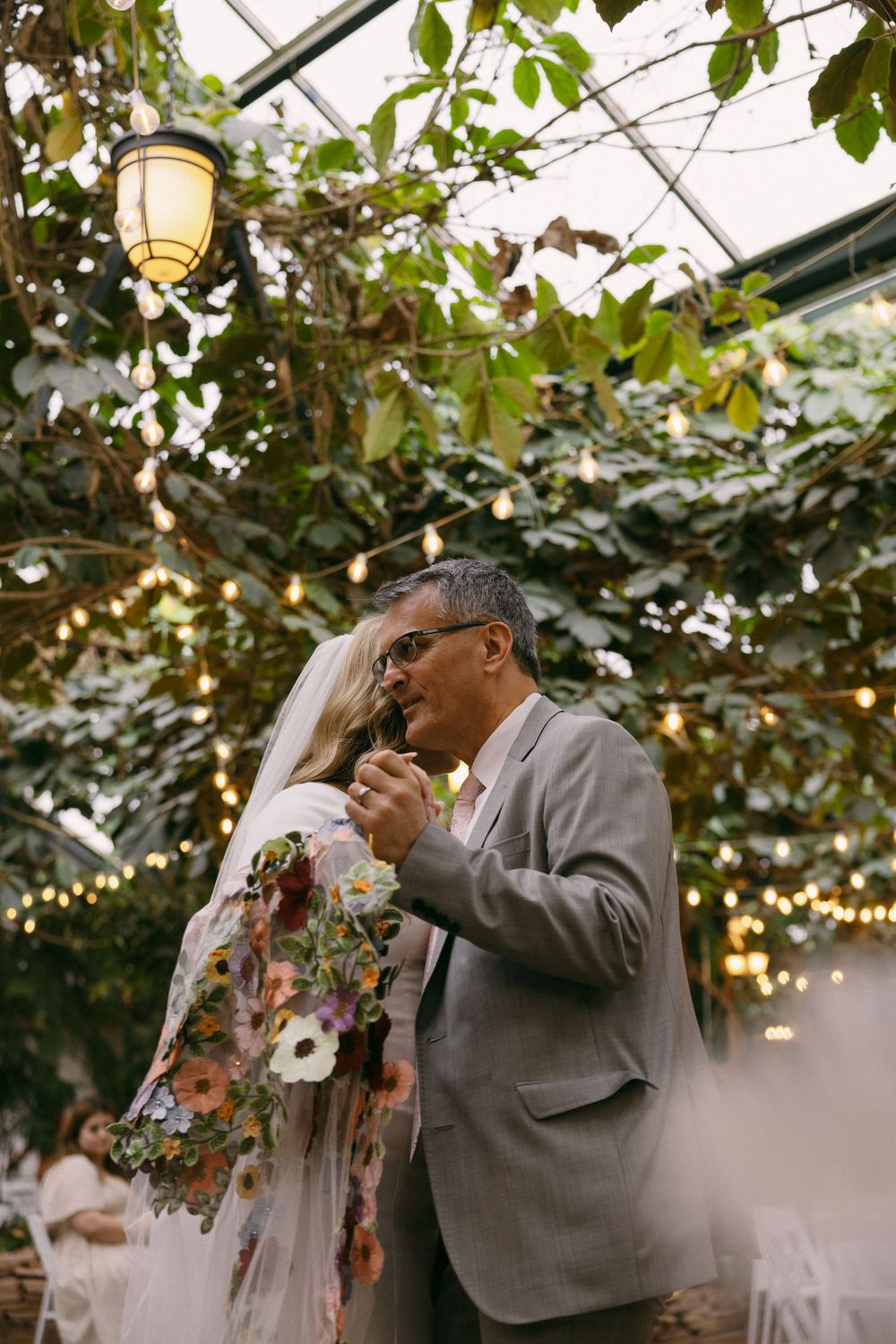 A tender dance moment beneath a garden pavilion strung with twinkling lights and lush greenery overhead.