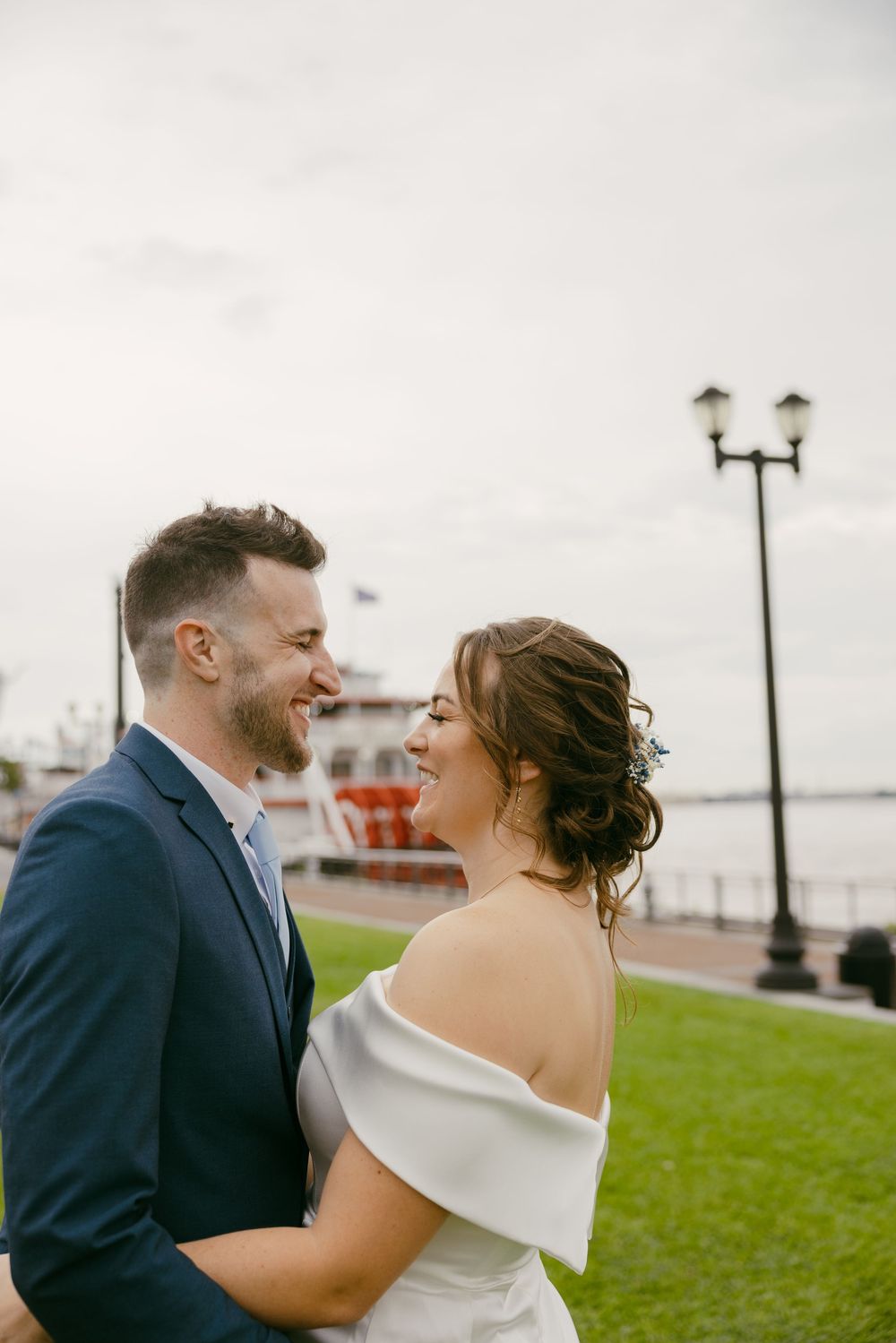 A couple shares a joyful moment together outdoors near a waterfront with a lamp post and boat visible in background.