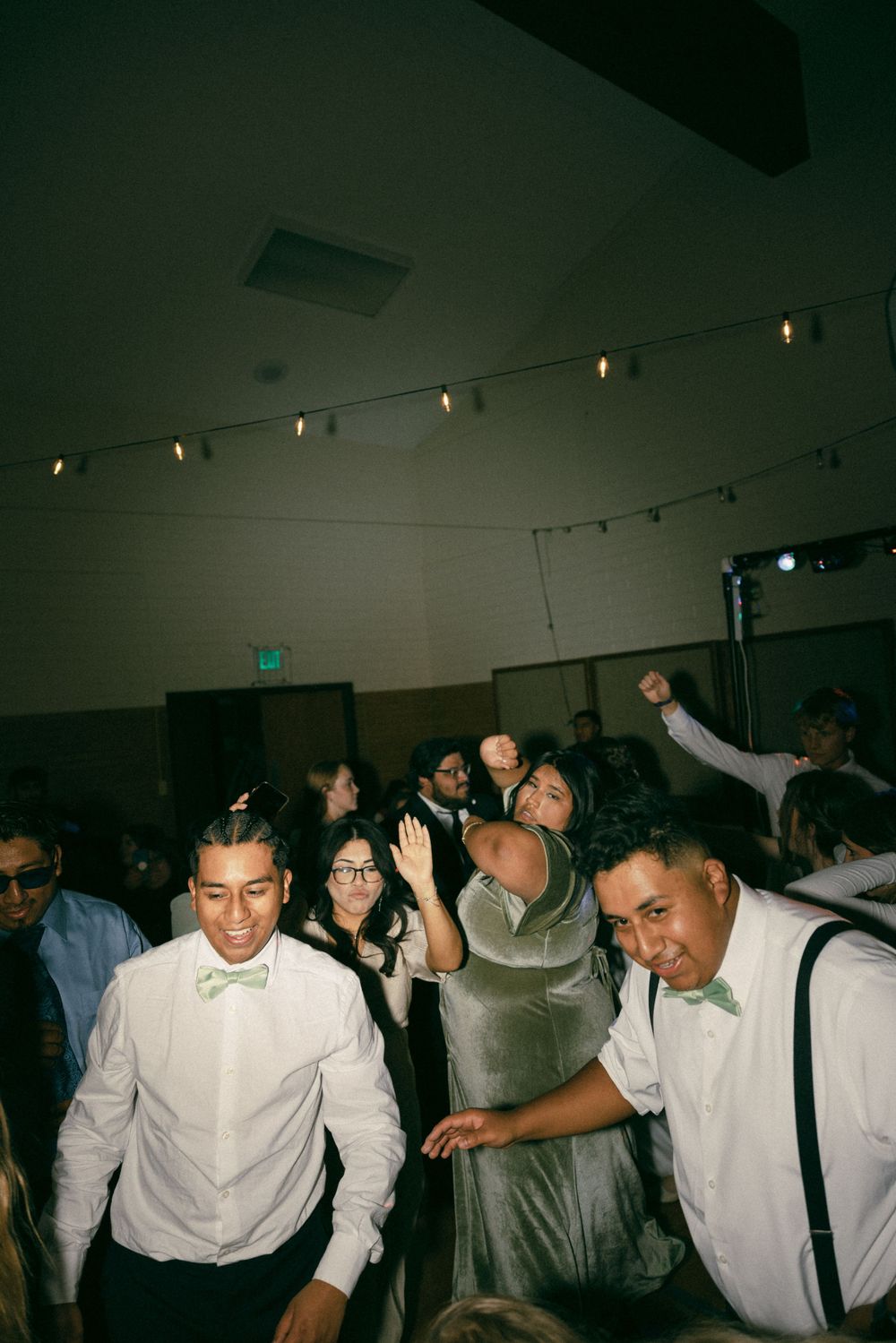 Wedding guests dancing and celebrating on a dance floor under string lights.