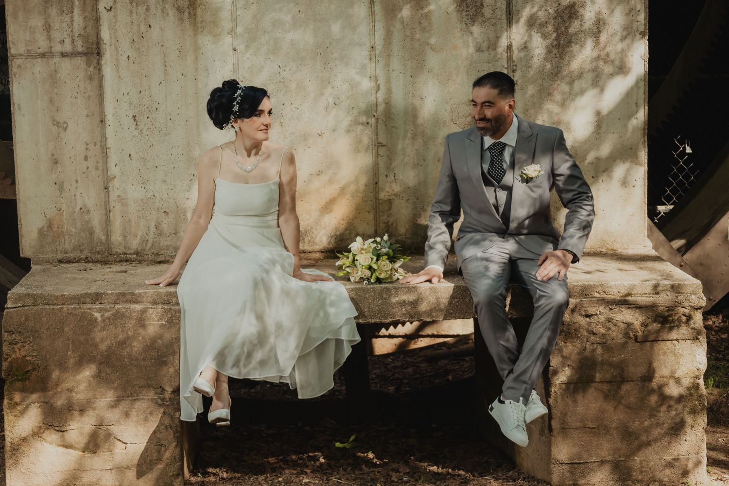 Romantic wedding couple poses against rustic stone wall in natural lighting.