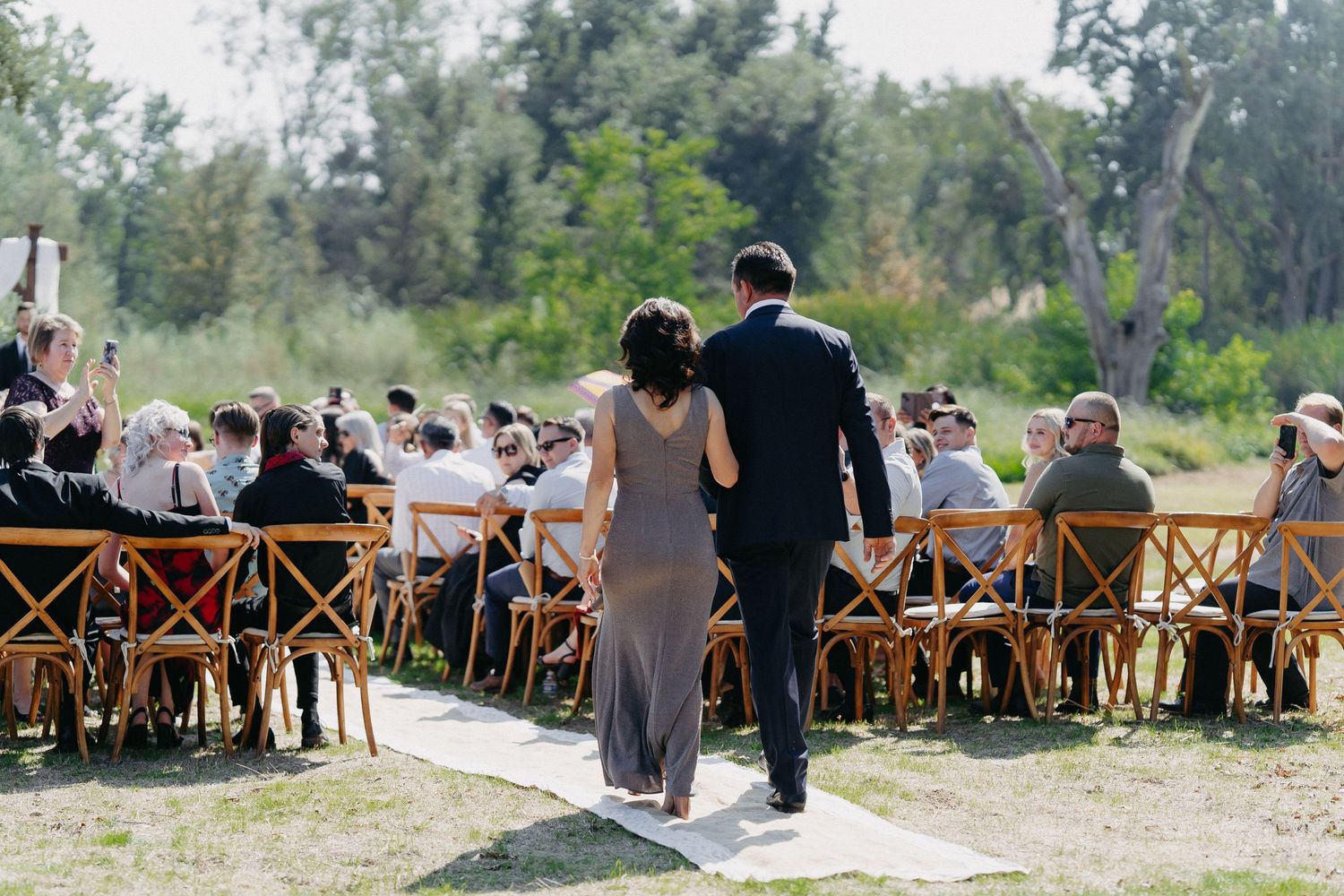 Wedding ceremony aisle with wooden cross-back chairs and white runner.