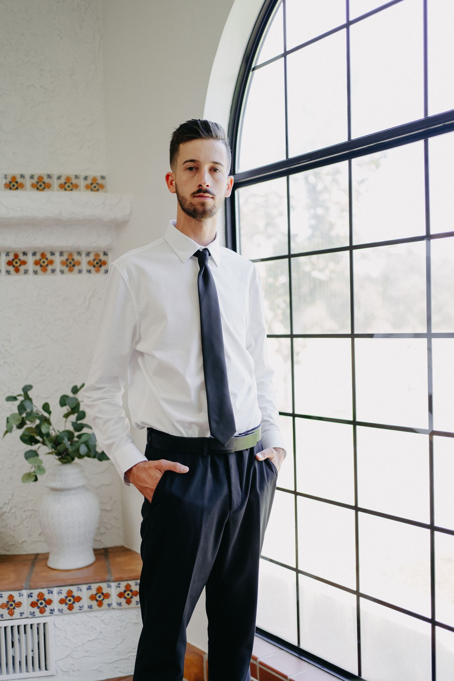 Professional portrait of man in business attire standing by large arched window.