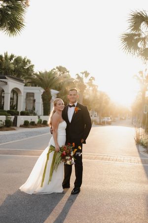 Wedding couple posing on a palm-lined street at sunset with golden light behind them.