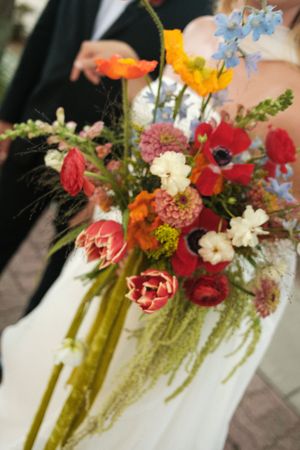Vibrant wedding bouquet featuring red, orange, and blue wildflowers against white fabric.