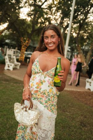 Person in floral dress holding a beverage at an outdoor summer event.