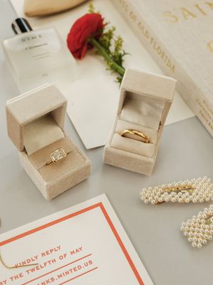 Wedding details featuring ivory invitation cards, pearl necklace, and ring boxes on white surface.
