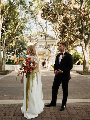 A wedding couple poses along a brick pathway with autumn trees in the background.