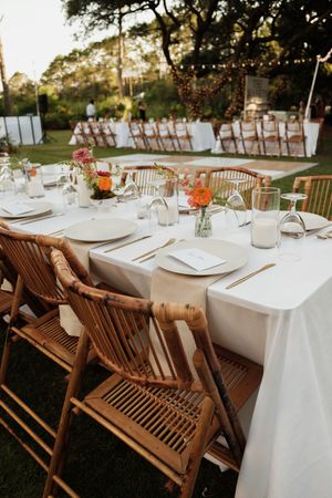 Wedding reception tables with white tablecloths and wooden chairs set up on a lawn.