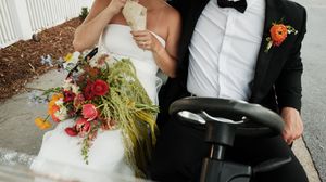 A romantic wedding couple embracing in formal attire with colorful floral bouquet details.