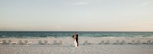 Silhouettes of a wedding couple walking along a serene beach at sunset.