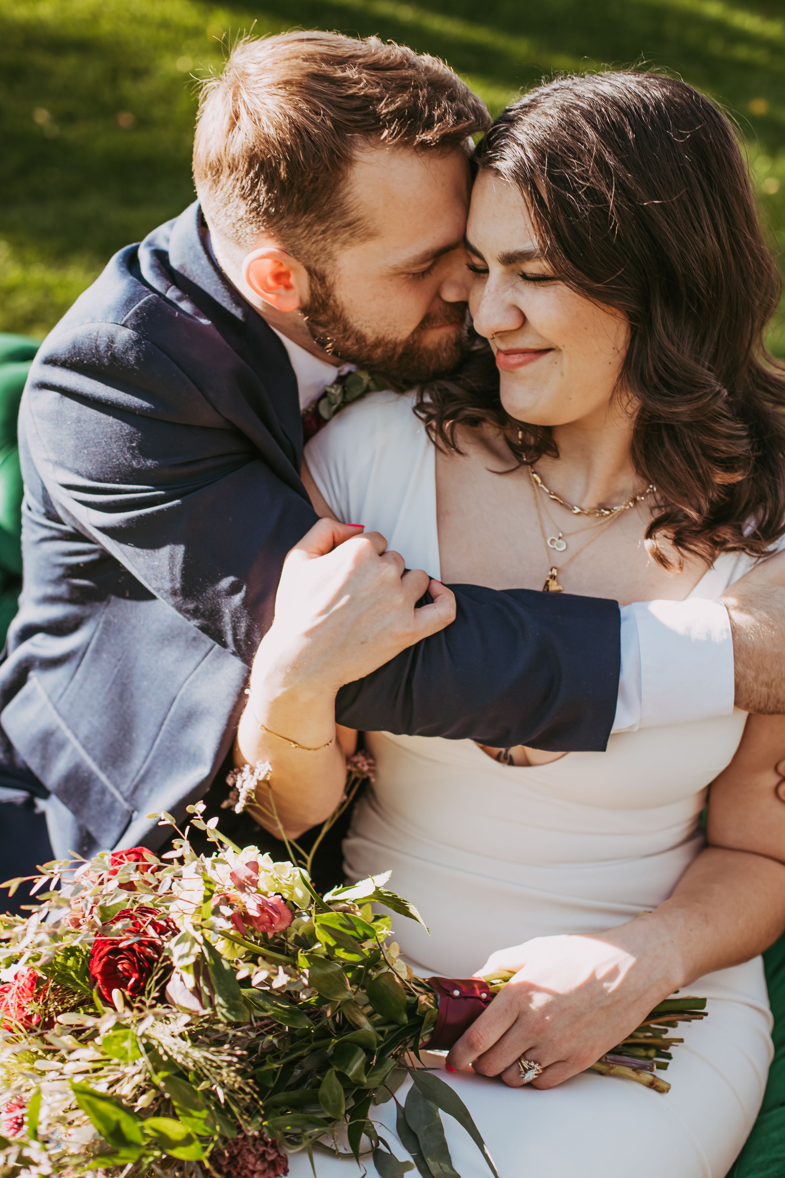 Wedding couple shares romantic moments on green lawn with floral bouquet.