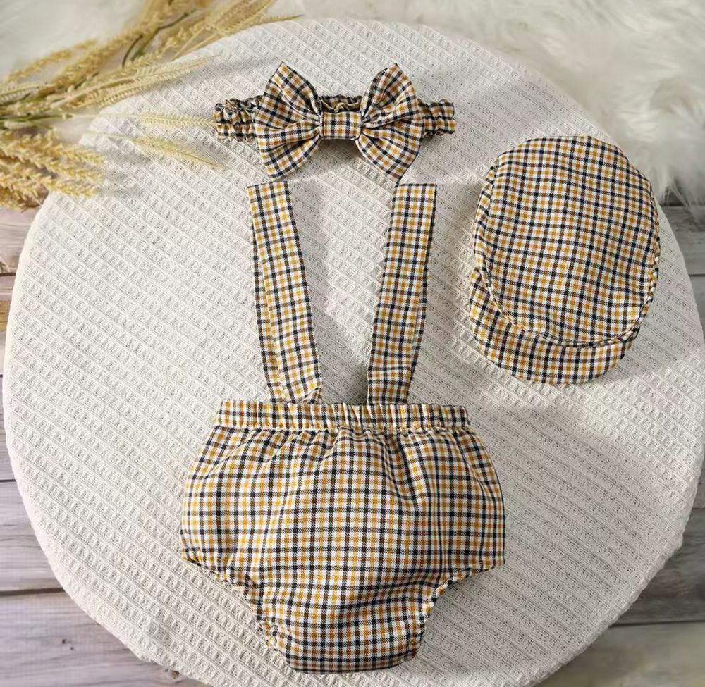 Vintage plaid baby set with bow headband, suspender bloomers, and matching cap on white textured surface.
