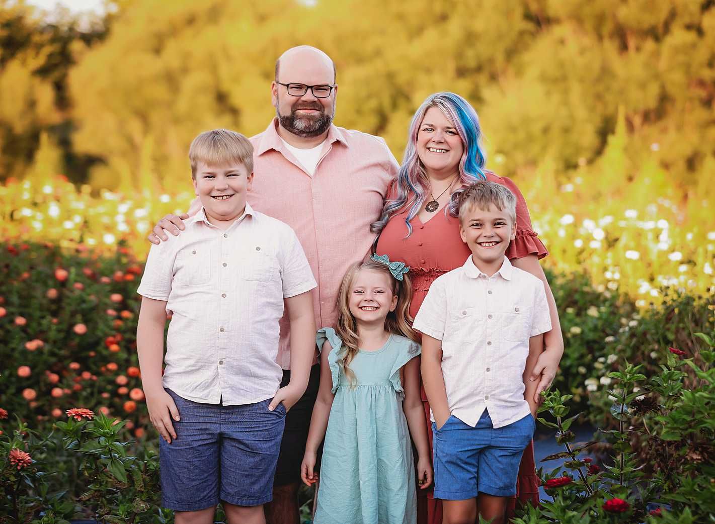 Family of five posing together in a field of yellow wildflowers during golden hour.