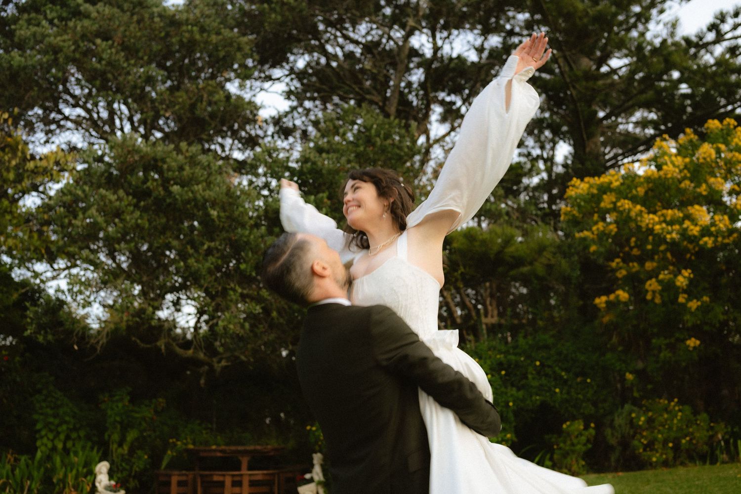Couple walks hand in hand through lush green garden setting.