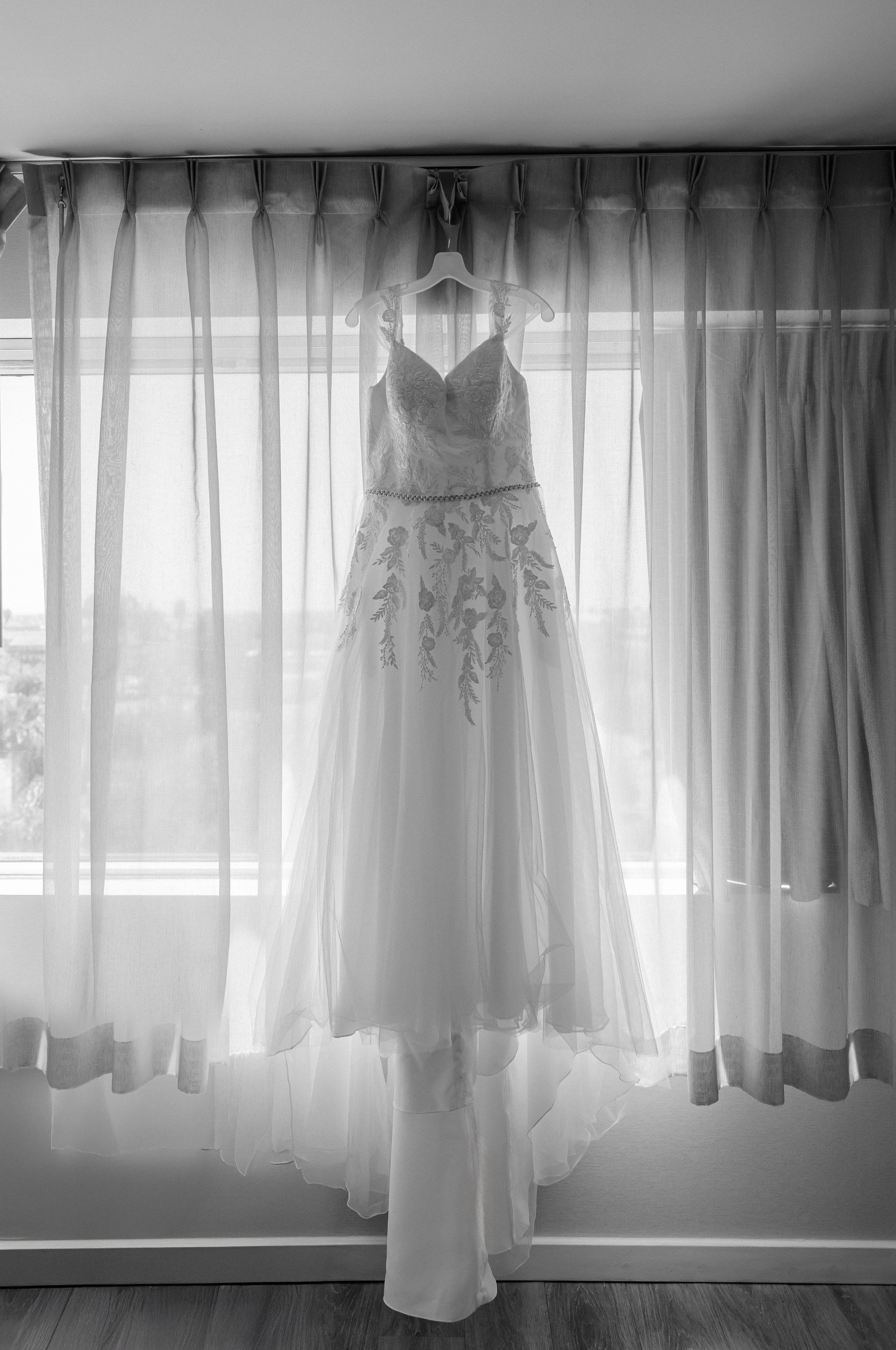 A series of delicate white wedding dresses hanging in front of sunlit windows creating a romantic silhouette effect.