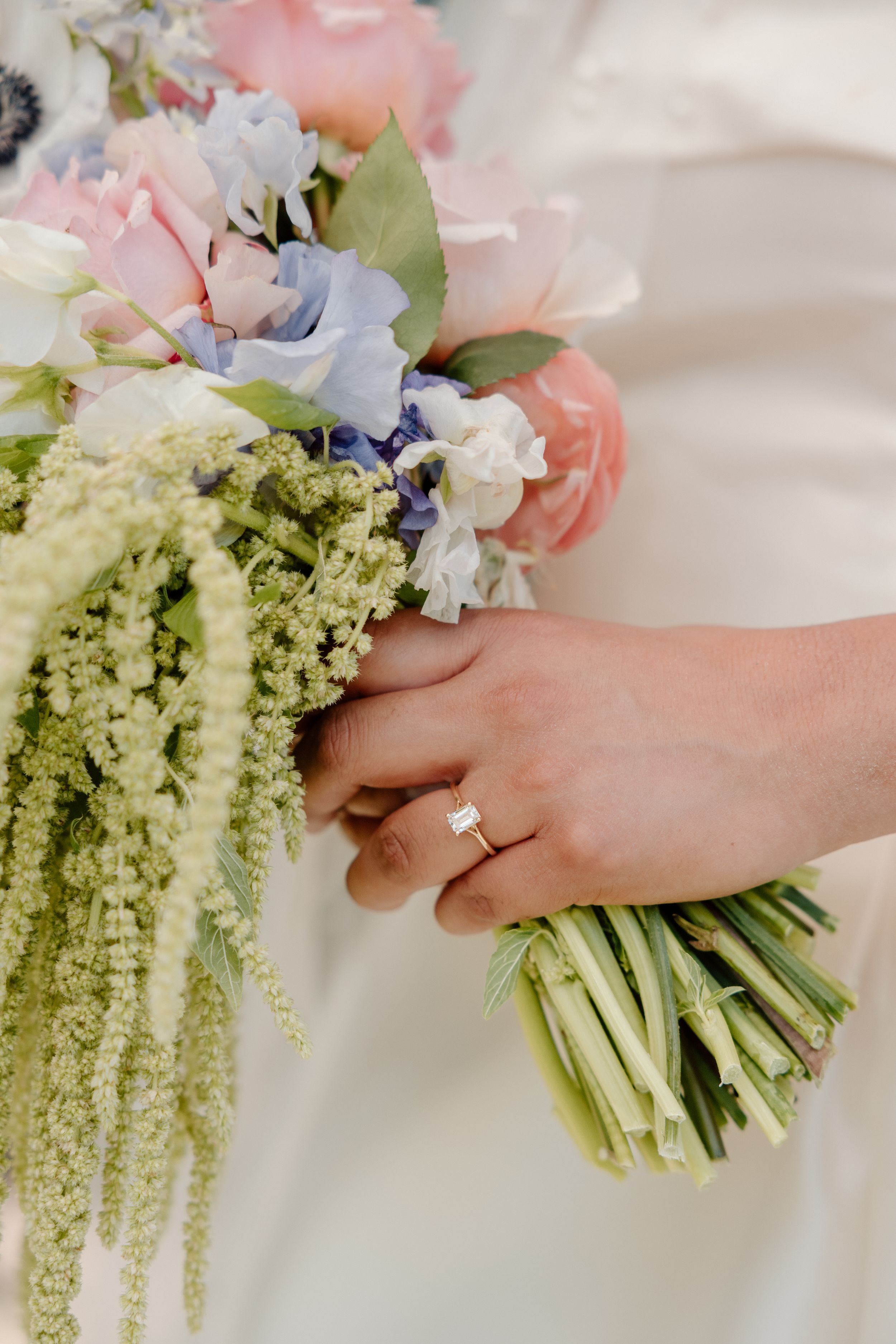 Wedding bouquet being tied with white ribbon featuring pastel flowers and green amaranthus in a cascading style.