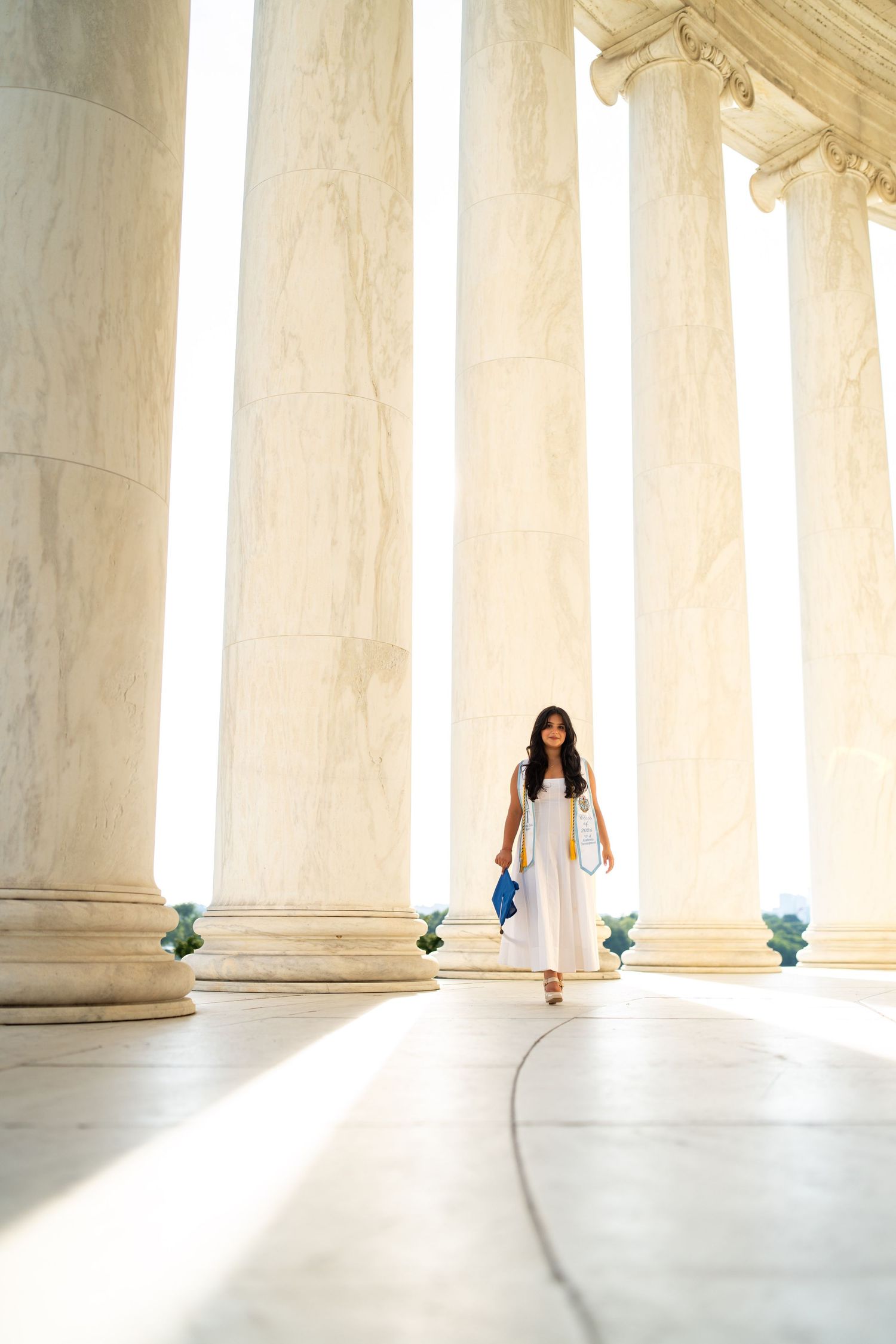 A woman in a white dress walks among tall marble columns at the Jefferson Memorial in Washington, D.C.