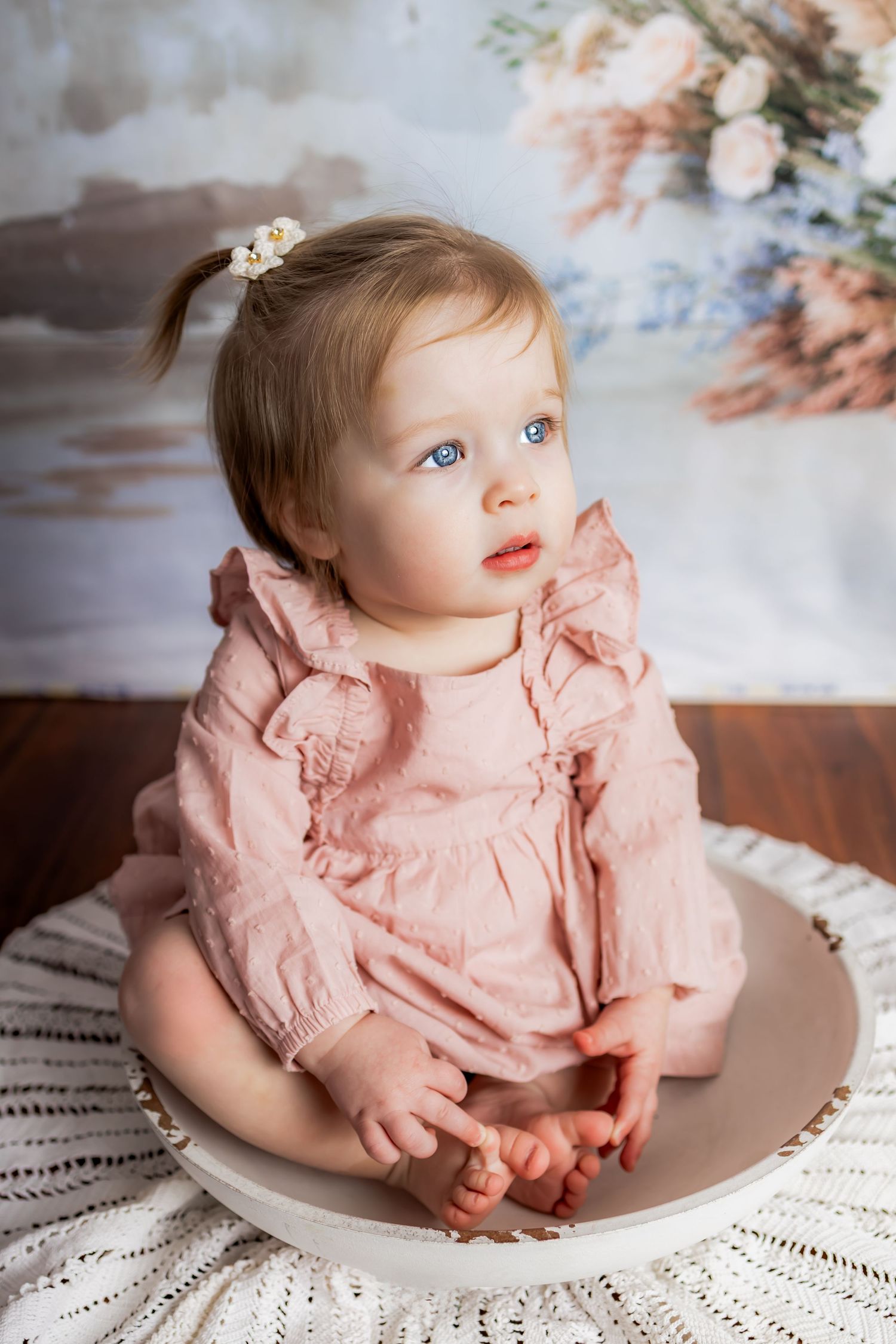 Adorable baby girl with blue eyes in pink ruffle dress sitting in a bowl on a white knit blanket. Milestone and cakesmash photographer RVA