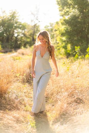 Woman in flowy gray maxi dress walks through golden sunlit field during sunset.
