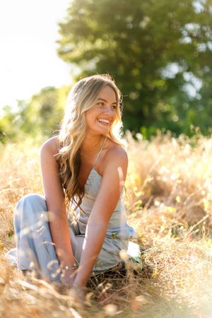 Woman in casual attire sitting in golden sunlit field during sunset with natural bokeh background.