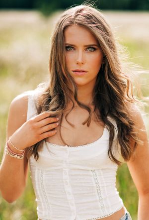 Portrait in a field showing long brown hair and white summer top with delicate details and warm lighting.