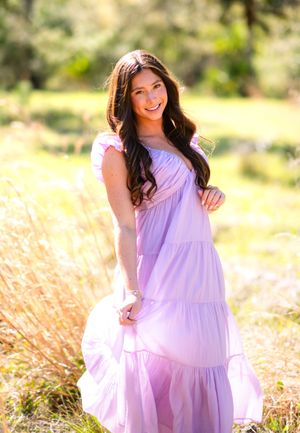 A person in a flowing lavender tiered maxi dress poses outdoors in a sunlit field with soft golden grass.