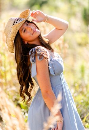 A dreamy summer portrait showing a light blue dress and straw hat against a sunlit meadow background.