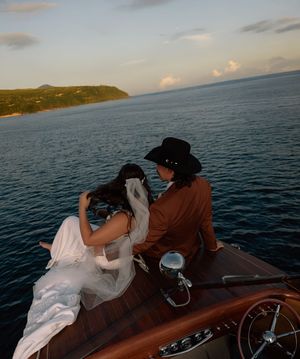 Romantic boat ride on calm waters at sunset with flowing white dress trailing behind.