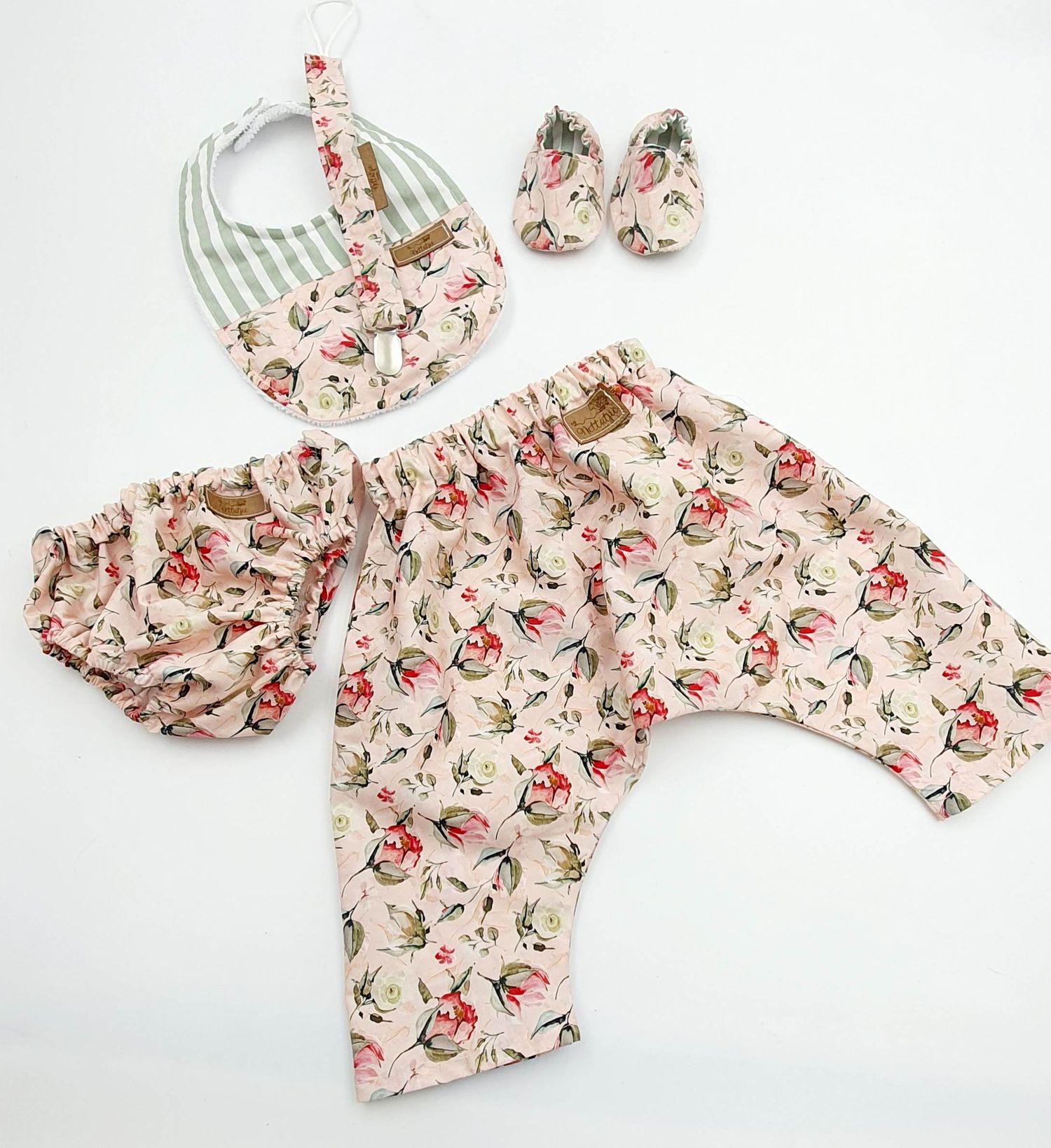 Floral print baby romper with matching accessories in pink and cream colors displayed on white background.