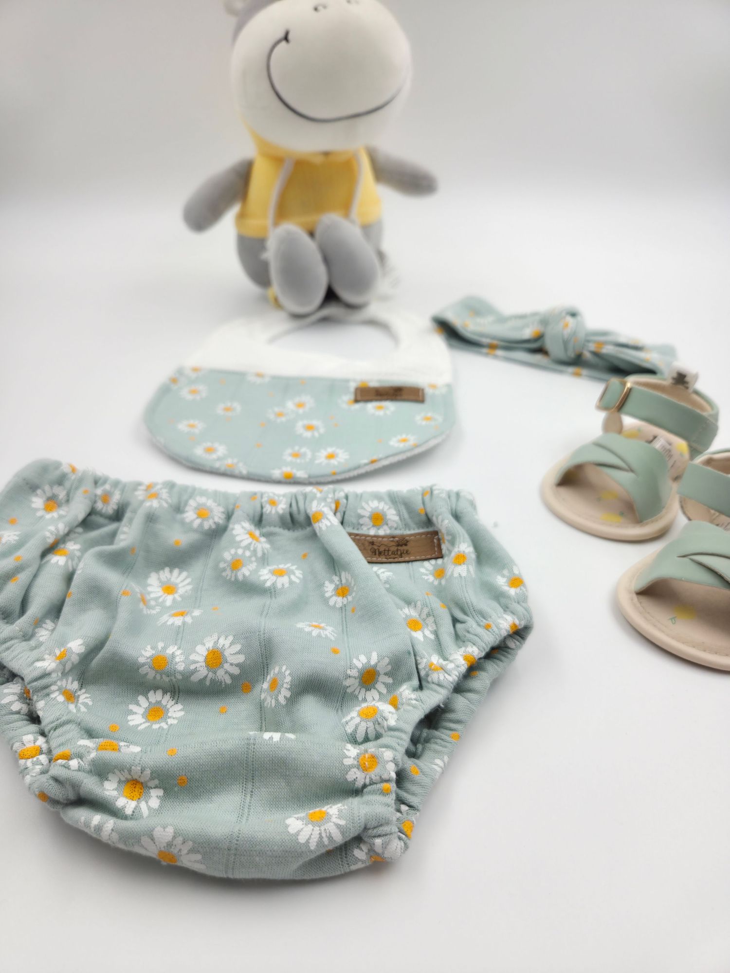Blue daisy print baby bloomers with matching shoes and accessories shown on white surface.