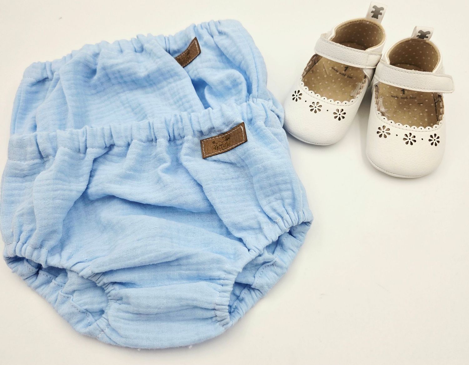 Light blue baby bloomers with white shoes displayed on neutral background.