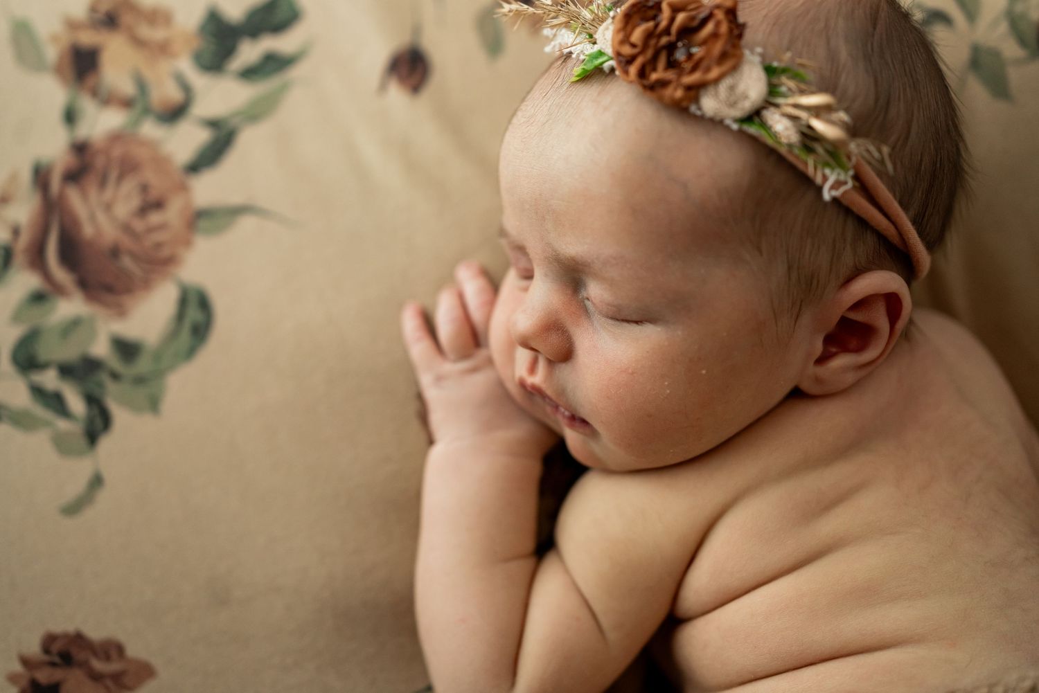 Sleeping newborn in orange knit wrap and floral crown resting in wicker basket.