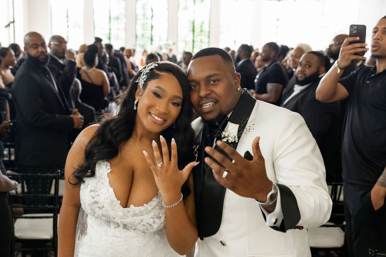 Newlyweds show off their wedding rings while taking selfies at their reception celebration.