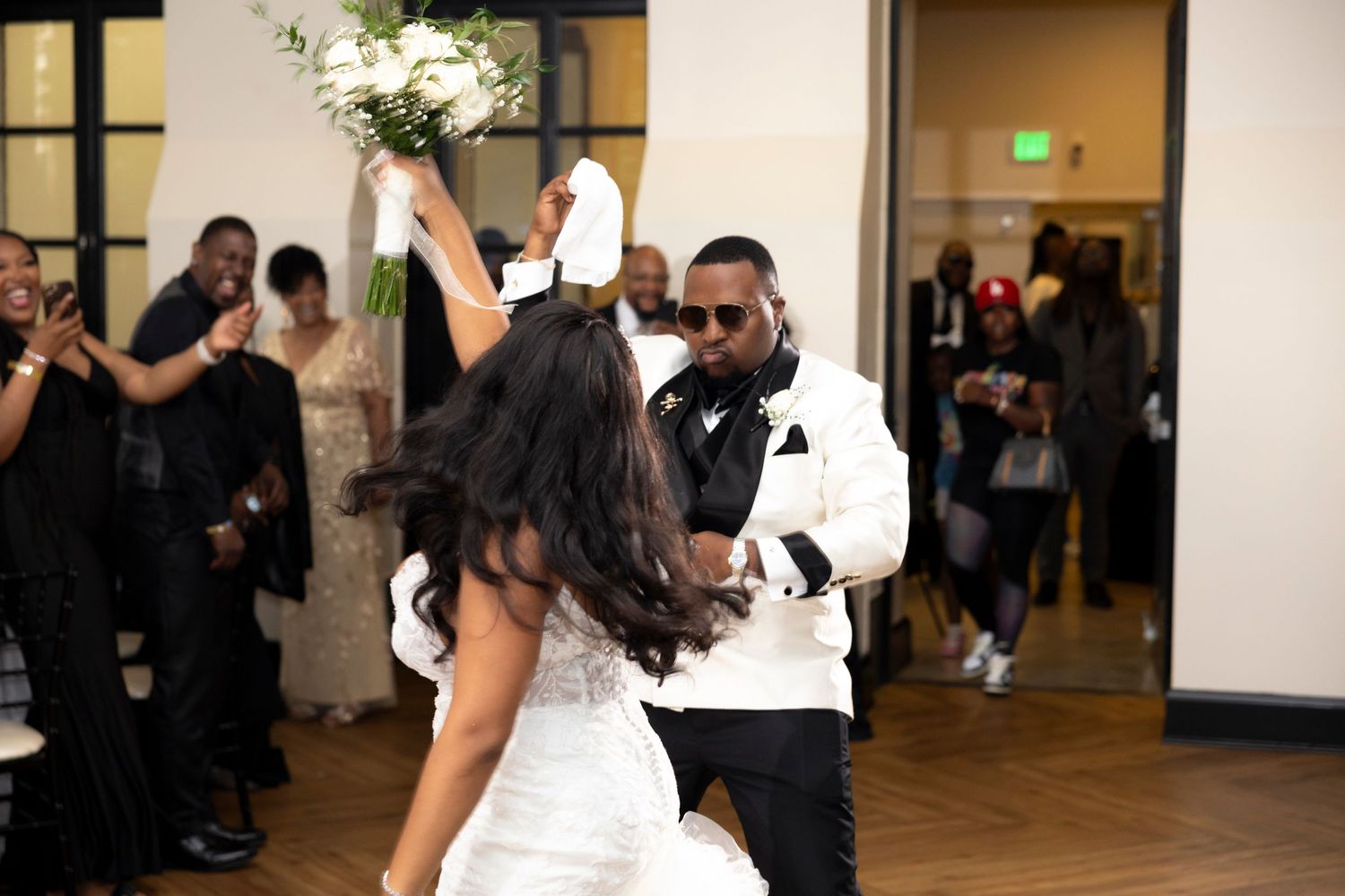 Newlyweds dance together at their wedding reception while guests watch from the sidelines in a ballroom.