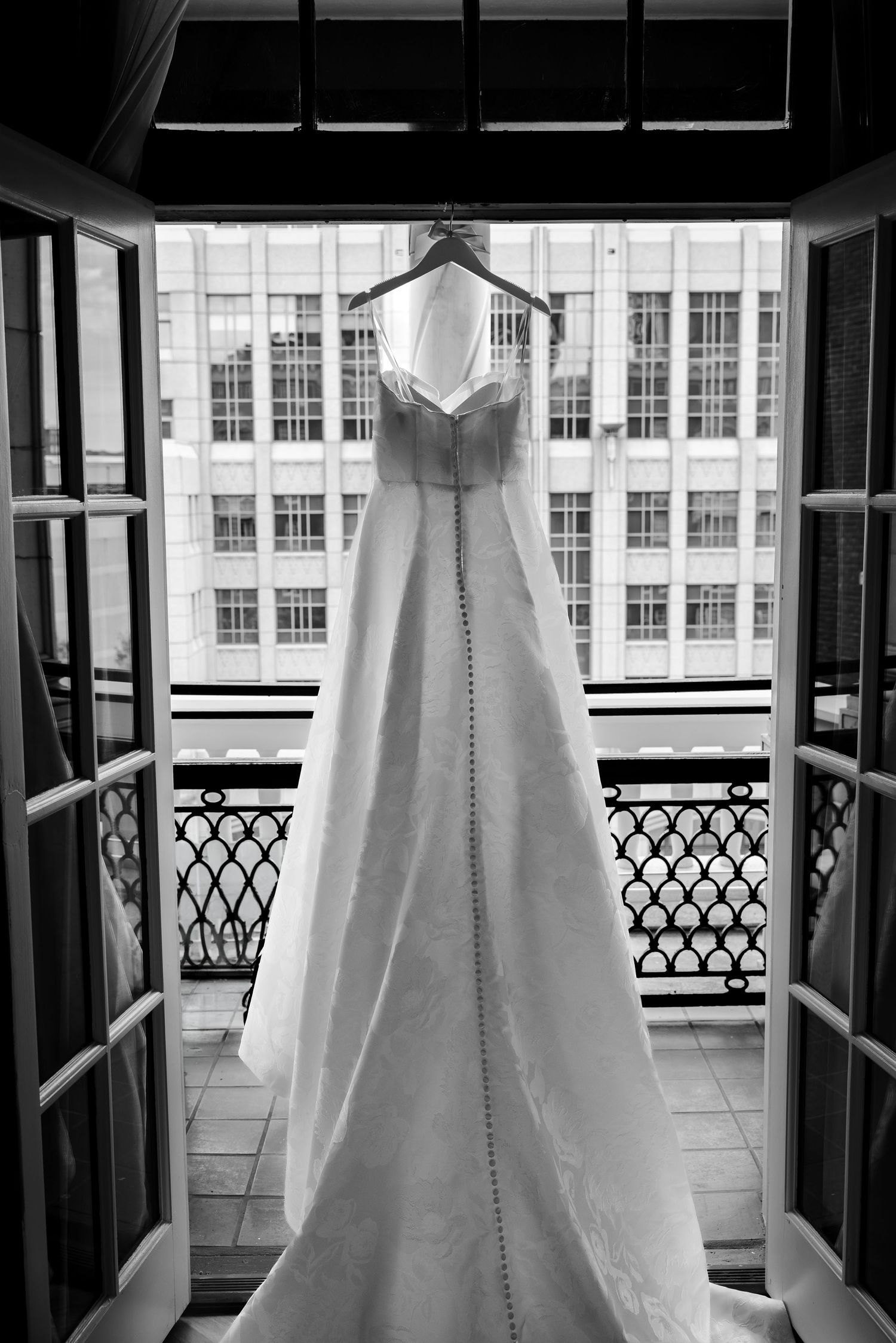 Elegant white wedding dress hanging on a hanger in an open balcony window, black and white photography.