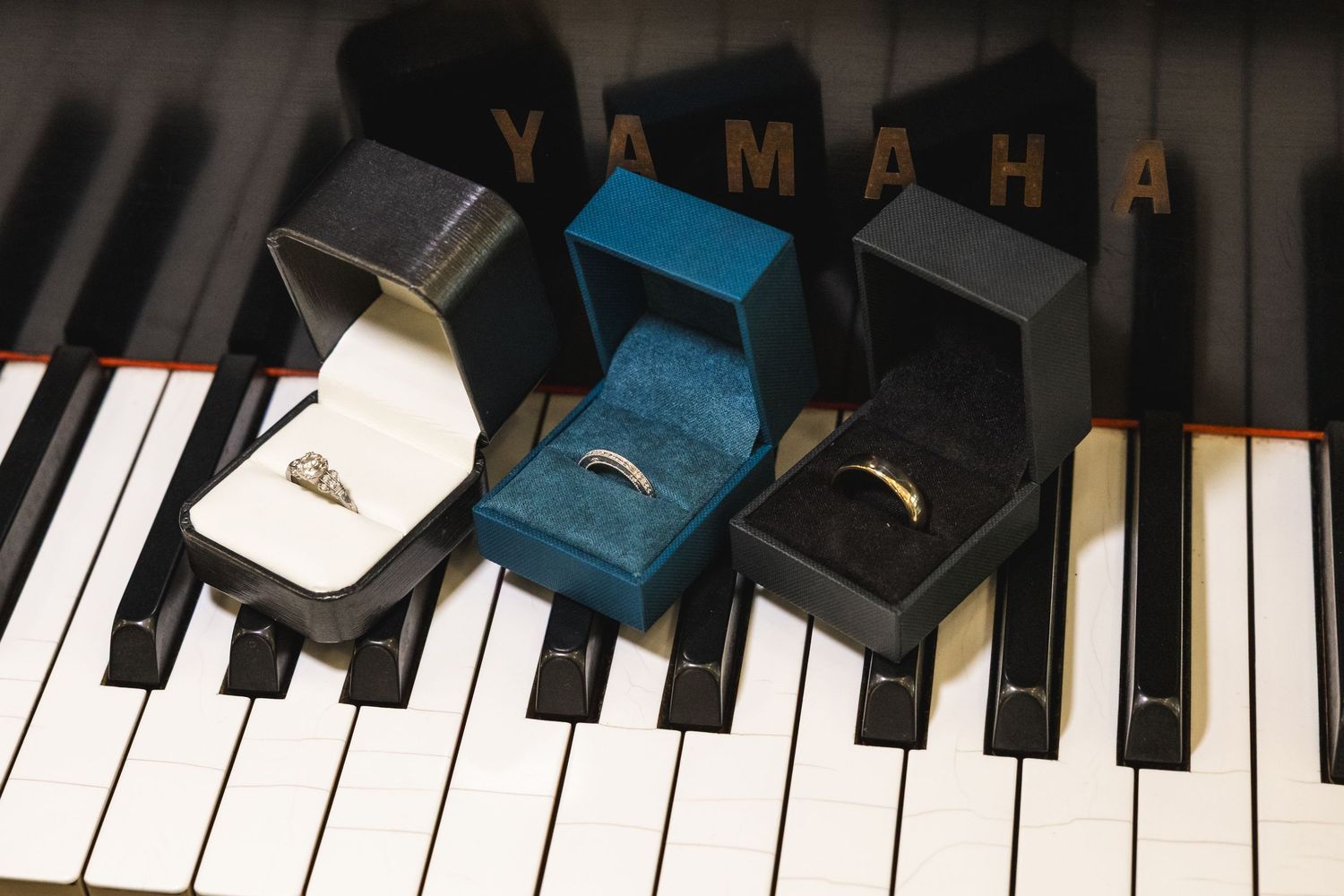 Three wedding rings in elegant boxes displayed on Yamaha grand piano keys, perfect for a romantic music-themed wedding.