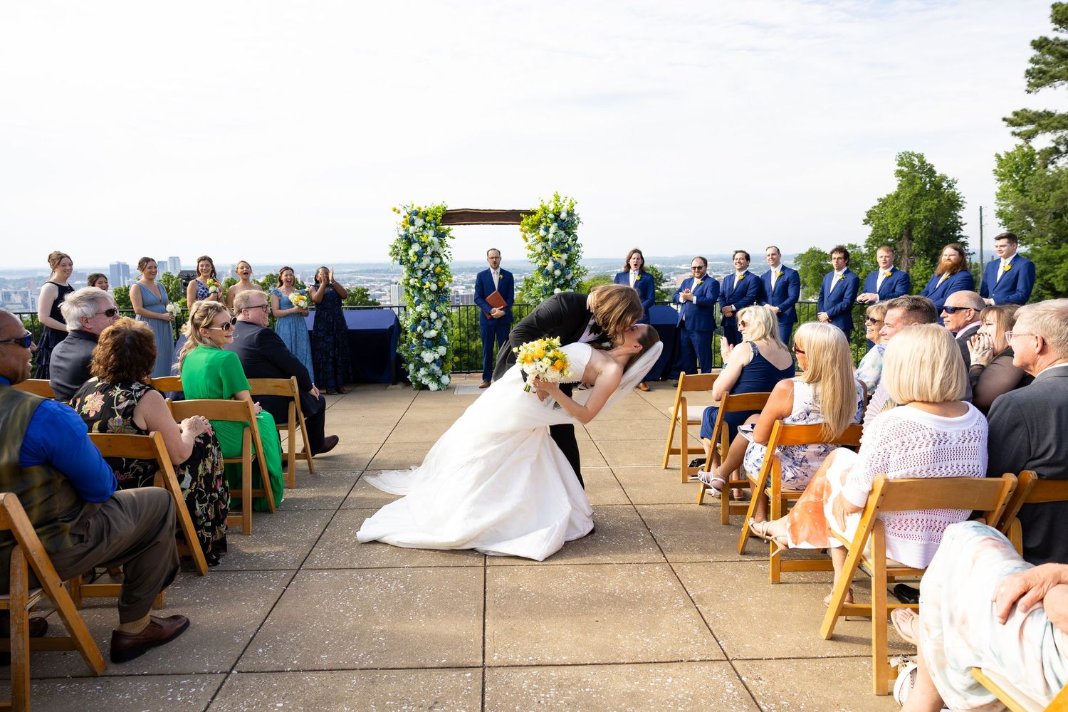 Bride walks down aisle at outdoor rooftop wedding ceremony with guests seated.