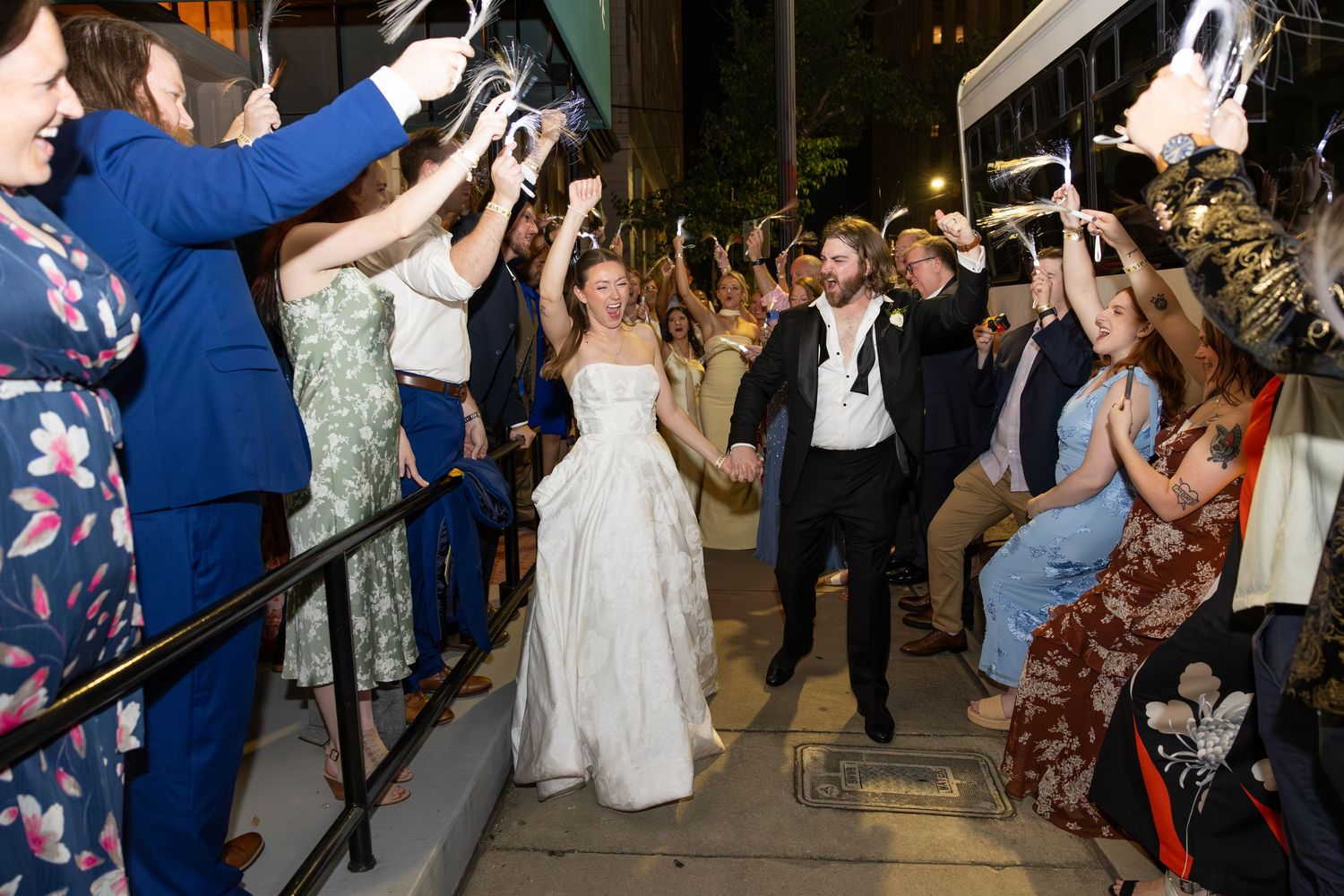Bride and groom exit wedding venue holding hands through cheering guests on decorated steps.