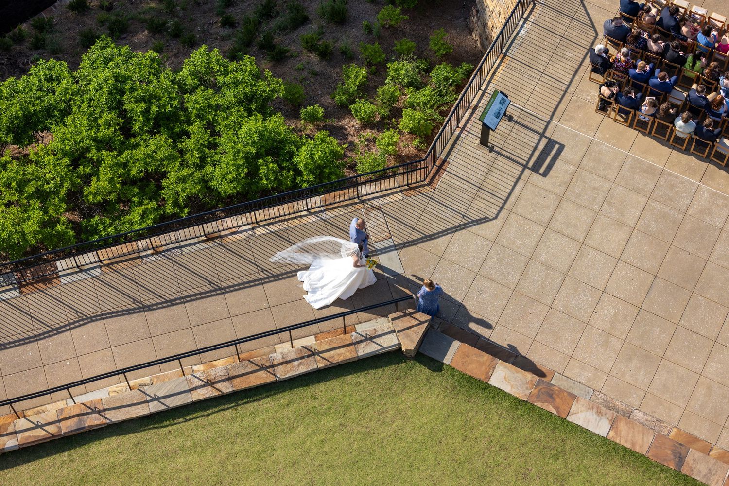 Aerial view of bride and groom walking on a patio pathway toward their outdoor wedding ceremony guests.