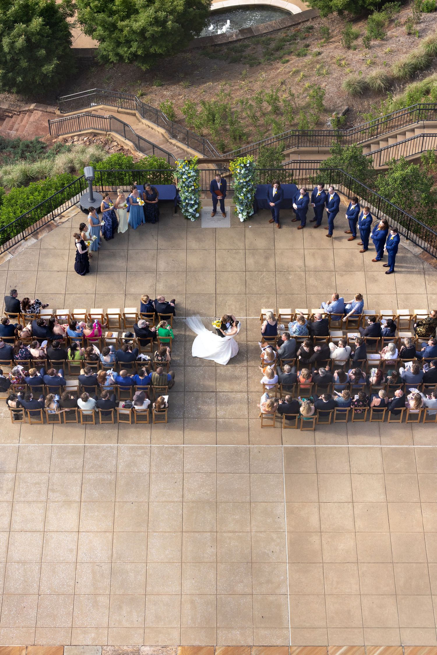 Aerial view of an outdoor wedding ceremony with guests seated in rows on a stone patio.