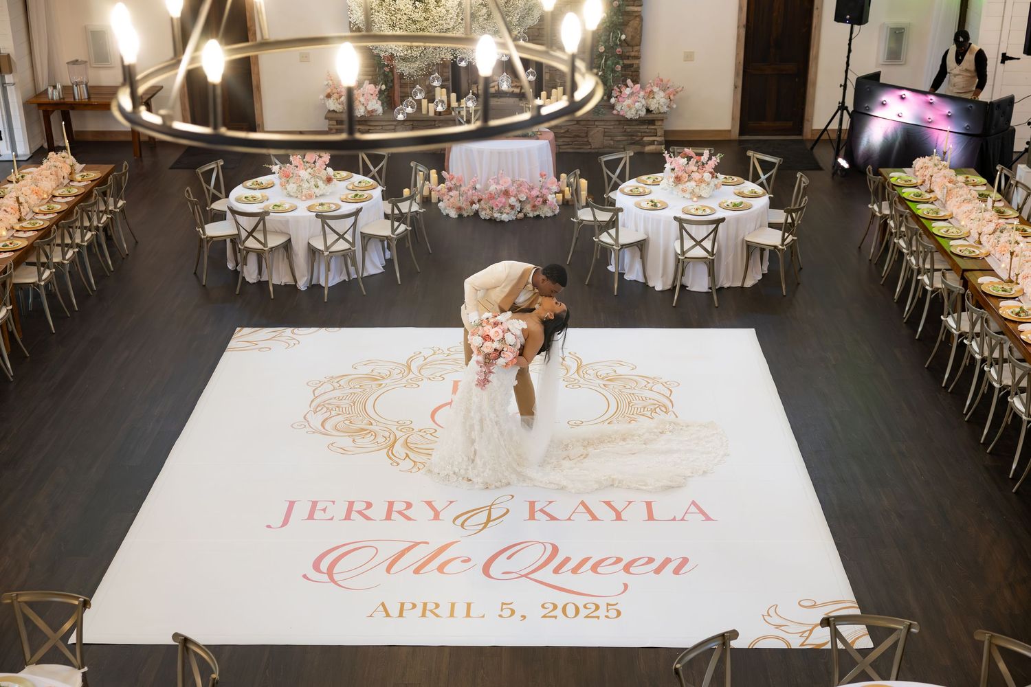 Bride and groom share first dance on custom monogram dance floor at elegant wedding reception with pink floral decor.