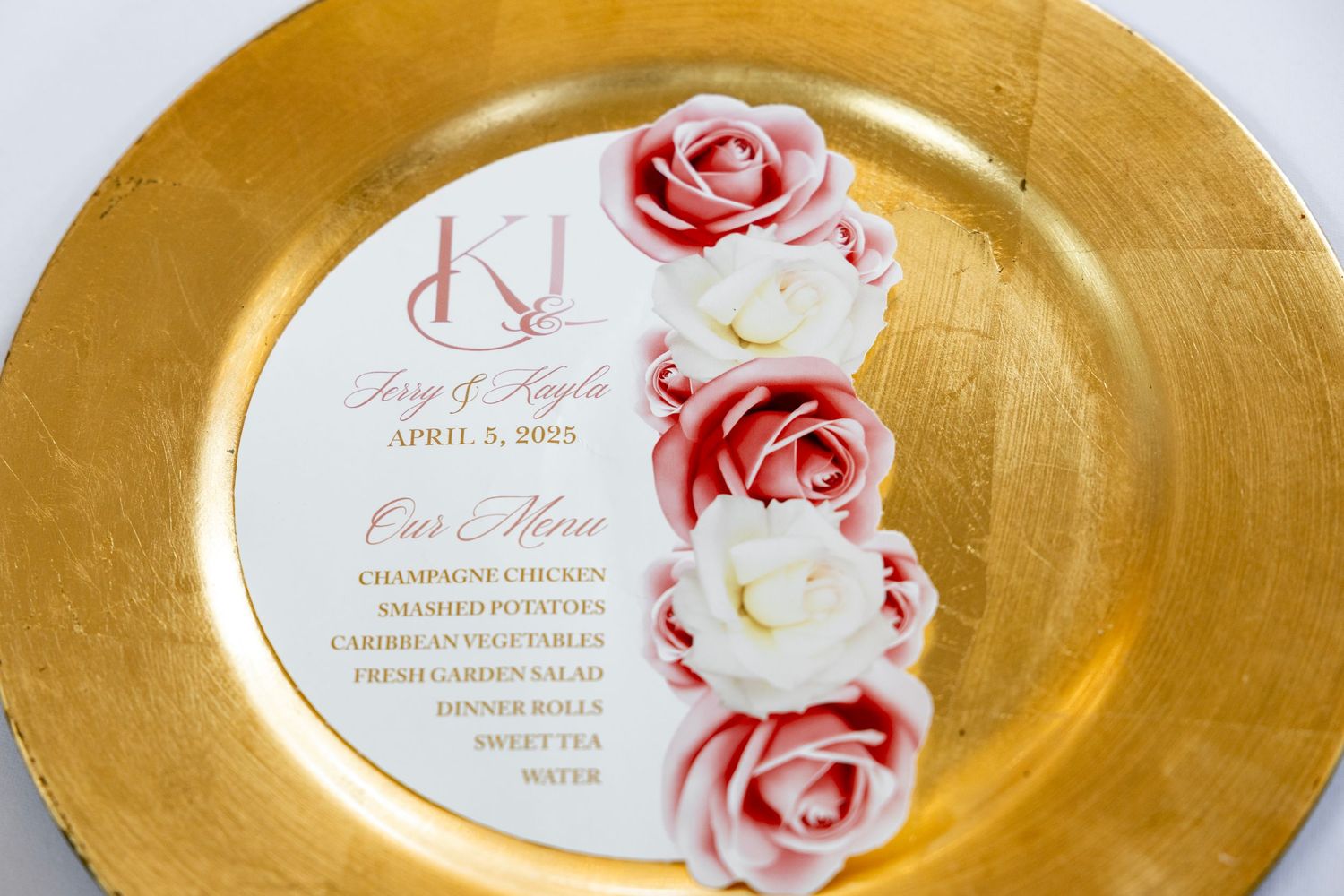 Gold charger plate with elegant wedding menu card featuring red and white roses, monogram K, and April 2025 date.