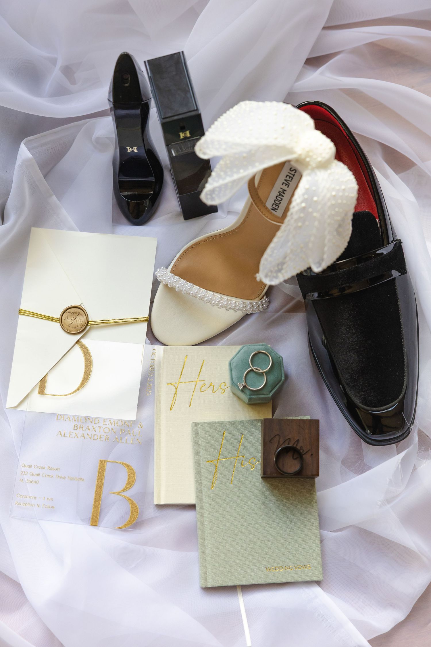 Wedding flat lay with bridal heels, groom loafers, gold-wax sealed invitations, his and hers vow books, and diamond rings.