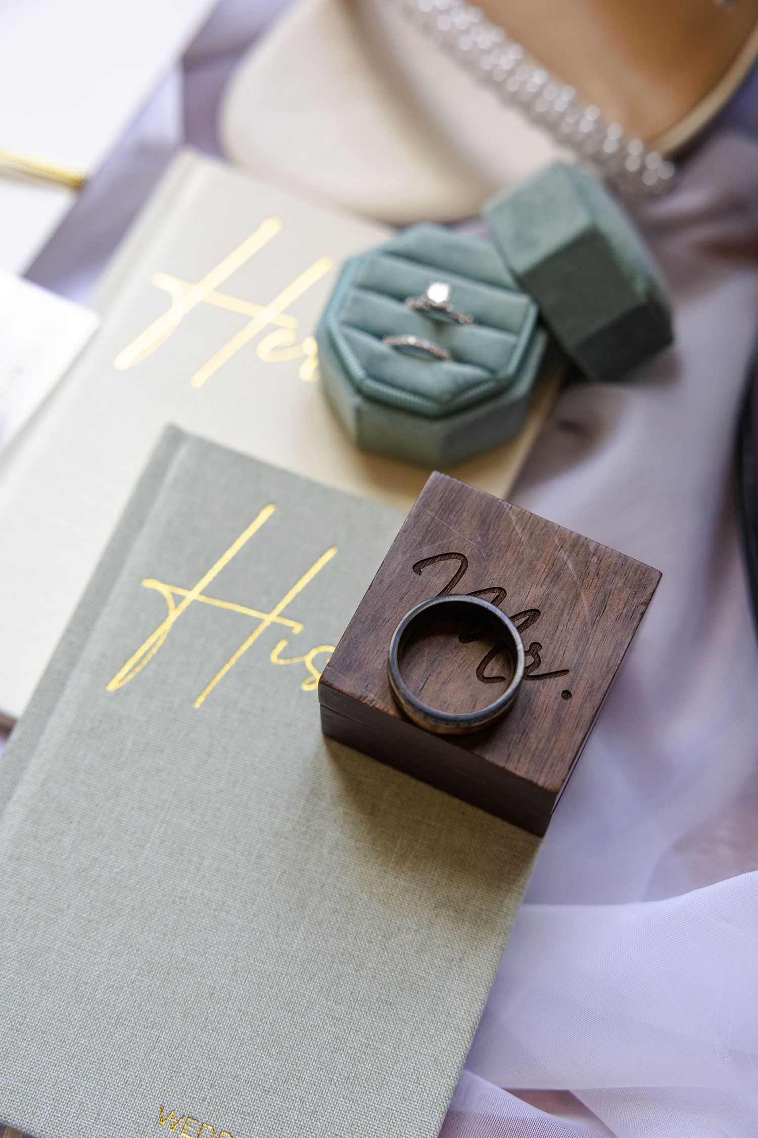 Wedding rings displayed in elegant boxes beside His and Hers vow books on a soft gray background.