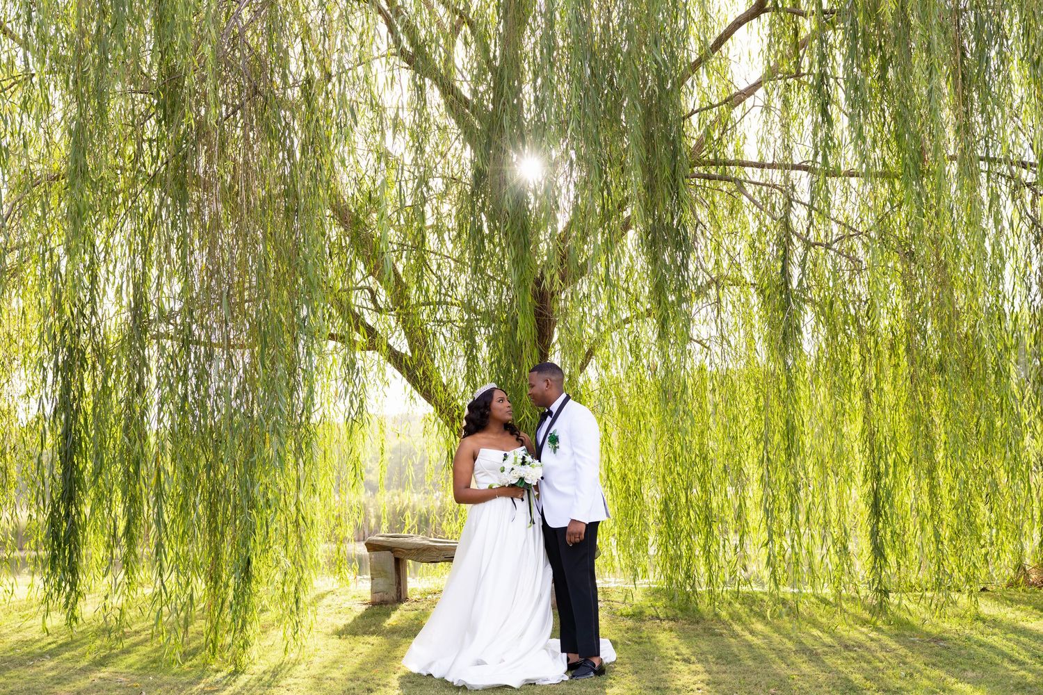 Bride and groom share a romantic moment under a weeping willow tree on their wedding day.