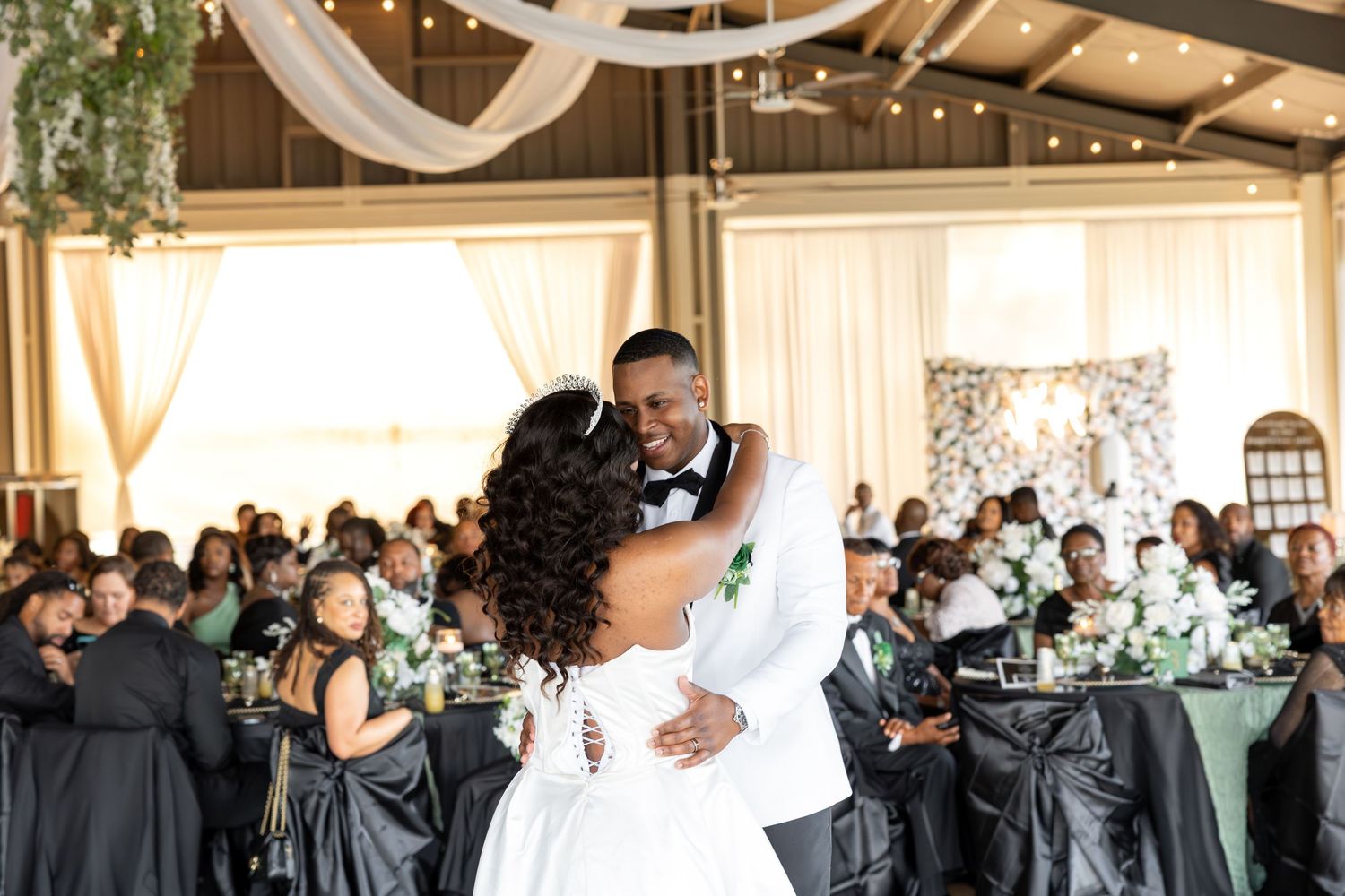 Bride and groom share their first dance at an elegant wedding reception with guests seated at decorated tables.
