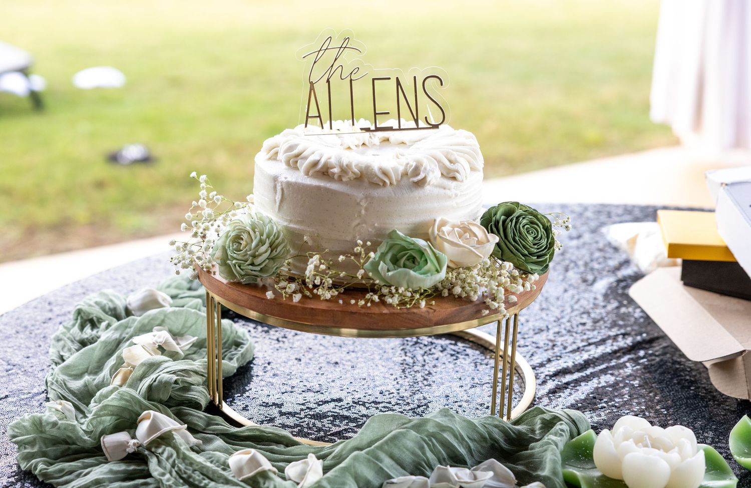 Elegant white wedding cake with succulent decorations and The Allens cake topper displayed on wooden stand.