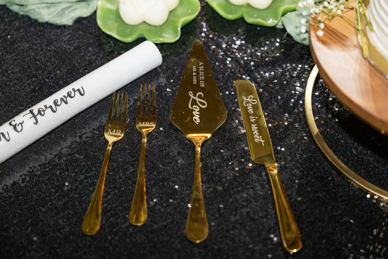 Gold engraved wedding cake server set with forks and knife on black glitter table.